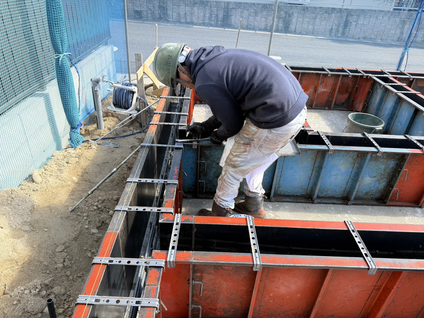 職人が立ち上がり型枠の締め付け金具を手作業で固定している様子